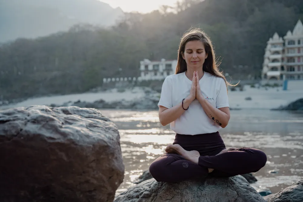 A student meditating on the rocks beside the Ganga at dusk