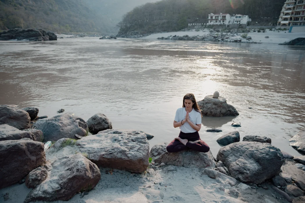 A student meditating on the river rocks below a Himalayan waterfall
